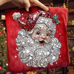 May include: A red Christmas pillow featuring a sparkling Santa Claus design. The Santa Claus image is made of numerous reflective, clear, and red crystals. The pillow has a soft, velvety texture and is decorated with small, sparkling stars.