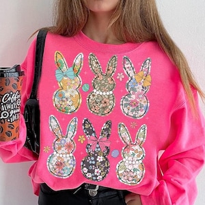May include: Pink sweatshirt with a floral pattern of six bunnies. The bunnies are all wearing bows and have a pearl necklace.