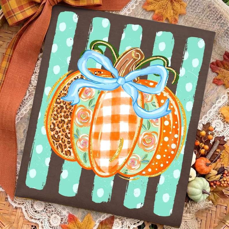 May include: A rectangular sign featuring a brown background with vertical light blue polka-dot stripes. Centered is a pumpkin illustration with segments of leopard print, orange gingham, and floral patterns, tied with a light blue ribbon bow.