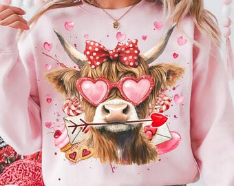 May include: Pink sweatshirt with a brown and white cow wearing heart-shaped sunglasses and a red polka dot bow. The cow is holding a red arrow with a heart on the end. The sweatshirt has a Valentine's Day theme.