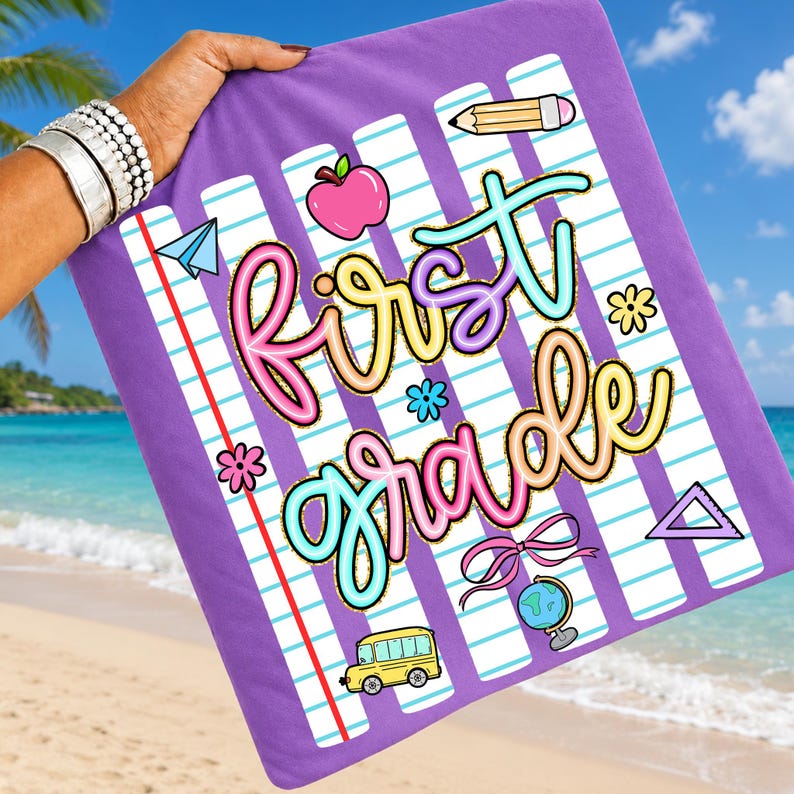 Peut inclure: Une serviette de plage violette avec un motif sur le th&egrave;me de l'&eacute;cole. La serviette pr&eacute;sente les mots "First Grade" dans des lettres color&eacute;es et fantaisistes, ainsi que des illustrations de fournitures scolaires telles qu'un crayon, une pomme et un bus scolaire. Le fond a un motif de papier lign&eacute;.