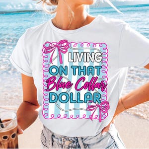 May include: White t-shirt with the text "LIVING ON THAT Blue Collar DOLLAR" in a pink and blue design. The design includes pink bows and a blue and white striped background.