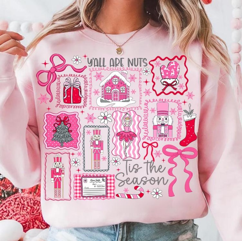 May include: A light pink sweatshirt with a festive design. The graphic includes pink illustrations of a gingerbread house, nutcrackers, a Christmas tree, and the text "Y'all Are Nuts" and "Tis the Season".