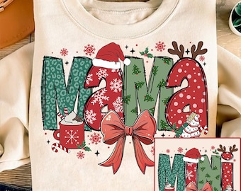 Op de afbeelding: Een crèmekleurige trui met een kerstthema. De woorden "Mama Mini" zijn geschreven in een feestelijk lettertype met rode, groene en witte accenten. Het ontwerp bevat een kerstmanmuts, sneeuwvlokken en een strik.