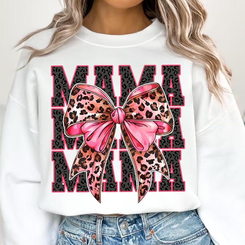 Pode incluir: Camisola branca com um la&ccedil;o rosa e um design de estampa de leopardo. O texto "MAMA" &eacute; repetido tr&ecirc;s vezes em preto e branco.