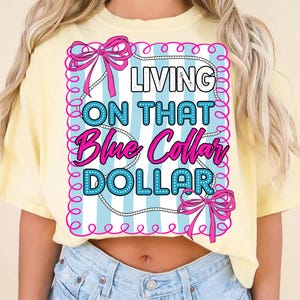 May include: A light yellow t-shirt with the text "LIVING ON THAT Blue Collar DOLLAR" in a pink and blue design. The design includes bows and a pearl necklace border.
