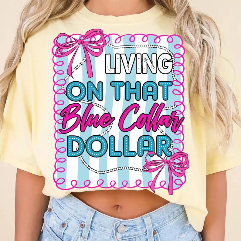 May include: A light yellow t-shirt with the text "LIVING ON THAT Blue Collar DOLLAR" in a pink and blue design. The design includes bows and a pearl necklace border.