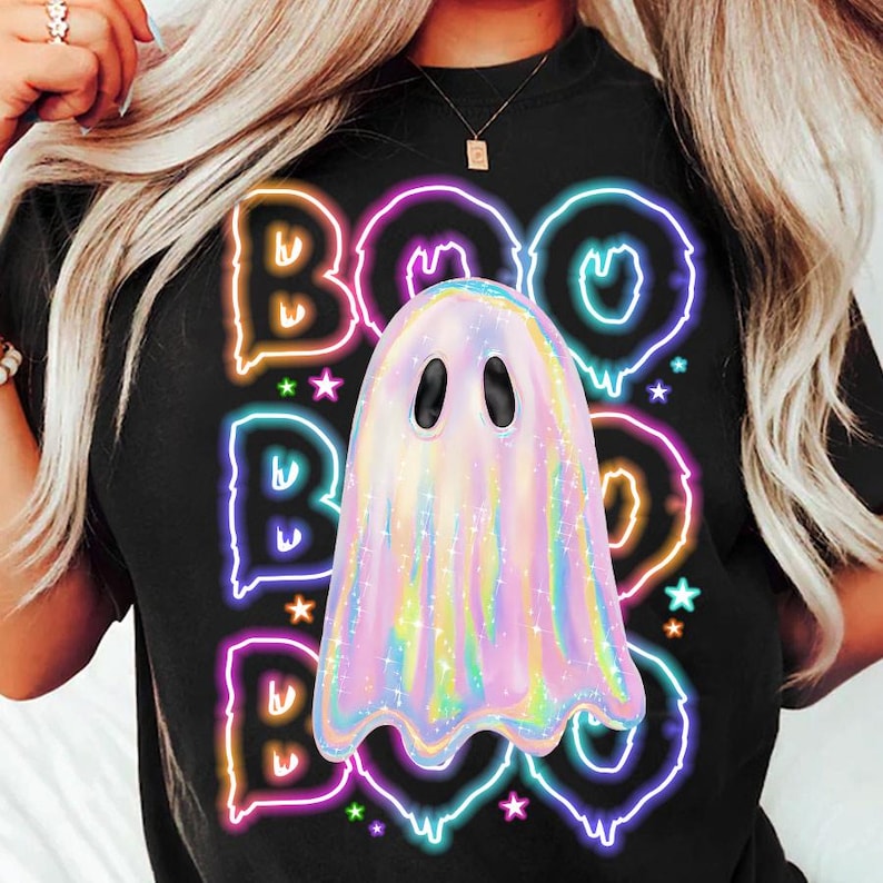 Pu&ograve; includere: T-shirt nero con un design "BOO" in stile neon e un fantasma pastello. Il design include stelle e un carattere stravagante, perfetto per Halloween. L'estetica generale &egrave; giocosa e festosa.