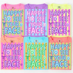 以下が含まれることがあります： 「HAPPY TO SEE YOUR FACE」の文字が縦縞模様でデザインされた、カラフルなTシャツ6枚。ピンク、紫、黄色、オレンジ、青の色合いです。テキストは星とスマイリーフェイスのアクセントが付いた遊び心のあるフォントです。