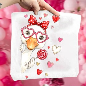 May include: White square pillow with a whimsical illustration of a goose wearing heart-shaped glasses and a red polka dot bow. The goose holds a lollipop, surrounded by heart-shaped accents in red, pink, and gold.