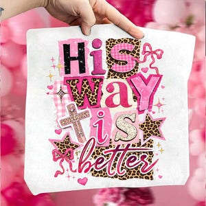 May include: A white tote bag with the text "His Way is Better" in a collage of pink, black, and leopard print patterns. The design includes a cross, stars, and hearts.