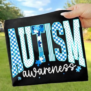 May include: Black fabric with the words "AUTISM awareness" in white and blue. The word "AUTISM" is in a bold, stylized font with puzzle piece and checkered patterns. The word "awareness" is in a cursive font.