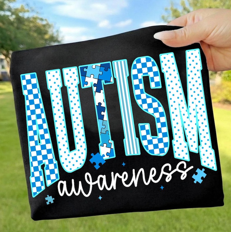 May include: Black fabric with the words "AUTISM awareness" in white and blue. The word "AUTISM" is in a bold, stylized font with puzzle piece and checkered patterns. The word "awareness" is in a cursive font.