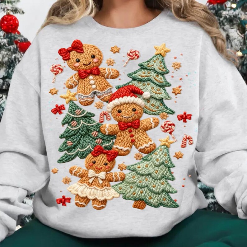 Op de afbeelding: Een lichtgrijze sweatshirt met een feestelijk kerstontwerp. Het ontwerp bevat peperkoekenmannetjes, kerstbomen, zuurstokken en ster- en strikaccenten. De peperkoekenmannetjes hebben rode strikken en hoeden. De bomen zijn groen en de zuurstokken rood en wit.