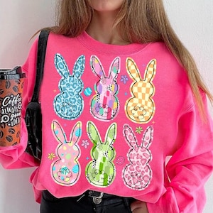 May include: Pink sweatshirt with a graphic of six colorful Easter bunny silhouettes. Each bunny is decorated with different patterns, including polka dots, stripes, and leopard print.