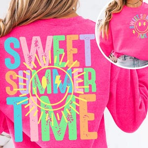 May include: Bright pink sweatshirt with the words "SWEET SUMMER TIME" in colorful, block letters. A yellow sun and a smiley face with a lightning bolt are in the center. The same design is repeated on the back of the sweatshirt.
