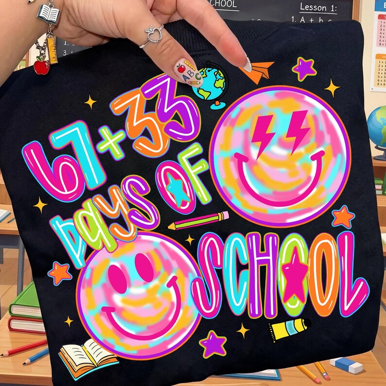 Może przedstawiać: Czarna bluza z kolorową grafiką. Projekt zawiera napis "67 + 33 DAYS OF SCHOOL" oraz dwie uśmiechnięte buzie z błyskawicami. Dodatkowo gwiazdki, oł&oacute;wki i globus.