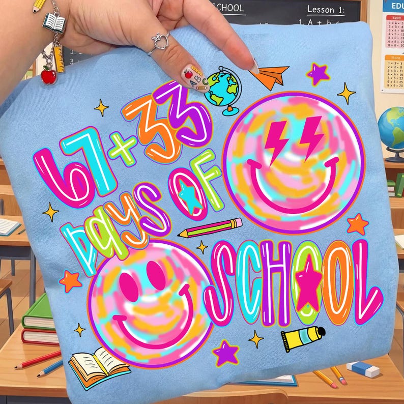 Może przedstawiać: Jasnoniebieska koszulka z napisem "67 + 33 DAYS OF SCHOOL" w jasnych kolorach. Projekt zawiera emotikony, gwiazdki, globus i przybory szkolne. Zabawny i kolorowy design dla uczni&oacute;w.
