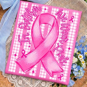 Op de afbeelding: Een rechthoekige stof met een roze en wit vichy-patroon met een grote, centrale roze bewustzijnslint. De tekst "In October We Wear Pink" is gedrukt in een gestileerd roze cursief lettertype, vergezeld van kleine roze lintpictogrammen en steraccenten.