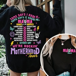 Puede incluir: Sudadera negra con un gr&aacute;fico rosa y blanco que dice "Some days I rock it. Some days it rocks me. Mama makes it all happen." El gr&aacute;fico enumera varias actividades como la lavander&iacute;a, la cocina, la tienda de comestibles, el trabajo, la pr&aacute;ctica, el patio de recreo, las vacaciones, los juegos deportivos, las excursiones, las fiestas de cumplea&ntilde;os. El gr&aacute;fico tambi&eacute;n incluye un rayo, un gesto de rock and roll y una mariposa. El texto "Either way we're rockin' Motherhood Tour" est&aacute; debajo de la lista de actividades.
