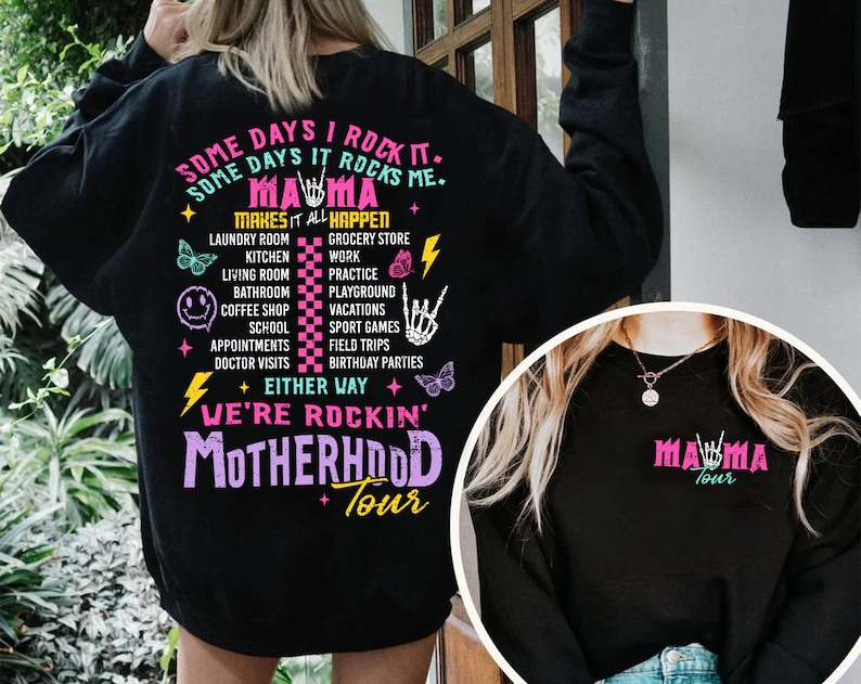 Puede incluir: Sudadera negra con un gr&aacute;fico rosa y blanco que dice "Some days I rock it. Some days it rocks me. Mama makes it all happen." El gr&aacute;fico enumera varias actividades como la lavander&iacute;a, la cocina, la tienda de comestibles, el trabajo, la pr&aacute;ctica, el patio de recreo, las vacaciones, los juegos deportivos, las excursiones, las fiestas de cumplea&ntilde;os. El gr&aacute;fico tambi&eacute;n incluye un rayo, un gesto de rock and roll y una mariposa. El texto "Either way we're rockin' Motherhood Tour" est&aacute; debajo de la lista de actividades.