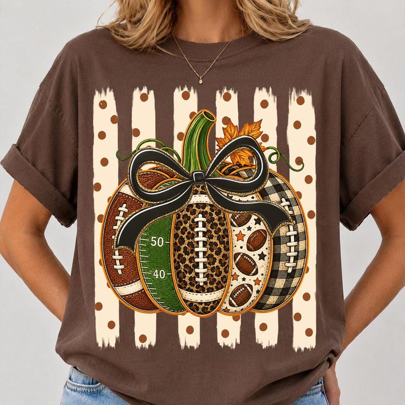 May include: A brown short-sleeve t-shirt featuring a graphic of a pumpkin composed of football-themed segments, including a green field section with 40 and 50 yard line markers, a leopard print section, and a black and white buffalo plaid section.