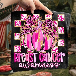 May include: Black blanket featuring a pink pumpkin with a leopard print bow and gold accents. The design includes pink ribbons and the words "Breast Cancer Awareness" in pink and white. The blanket is held up by a hand.