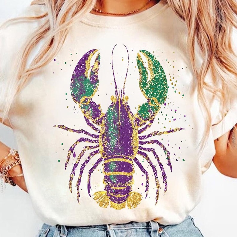May include: A white t-shirt with a purple and green glitter lobster design. The lobster is outlined in gold glitter.