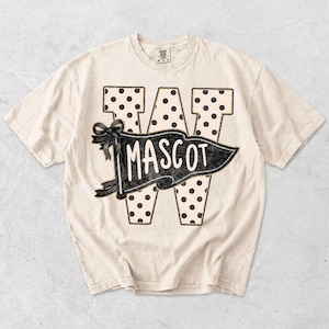 May include: A cream-colored short-sleeve t-shirt featuring a large letter W with a black polka dot pattern. Overlaid on the letter is a black pennant flag graphic with a bow on the left side and the word MASCOT printed in white capital letters.