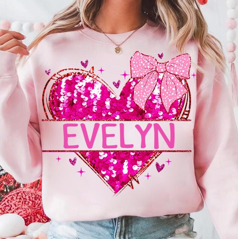 May include: Pink sweatshirt with a sequined heart and a pink bow. The heart has the name "EVELYN" written across it.