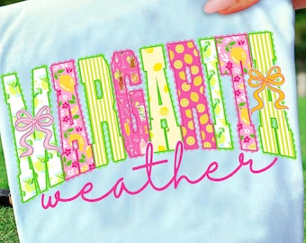 May include: Light blue t-shirt with the words "Margarita Weather" in a colorful, decorative font. The letters are filled with patterns of lemons, cocktails, and flowers, with a pink bow on each side.