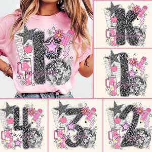May include: Pink t-shirt with a graphic design featuring the word "Preschool" in a glittery font, a disco ball, stars, flowers, and a pencil. The design also includes a tumbler with a floral pattern and an apple.
