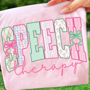 Puede incluir: Una camiseta rosa claro con las palabras "SPEECH THERAPY" en una fuente decorativa. Las letras est&aacute;n delineadas en verde y rellenas con varios patrones, incluyendo rayas, estampados florales y cuadros. Lazos rosas acent&uacute;an el dise&ntilde;o.