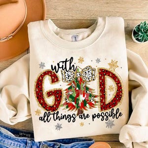 Op de afbeelding: Een crèmekleurige trui met een kerstboomontwerp en de tekst "with God all things are possible". De boom is versierd met een rode strik en rode en groene kerstballen. De letters zijn omrand met goud en hebben een luipaardprint.