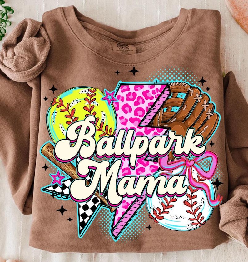 Puede incluir: Sudadera marr&oacute;n con un dise&ntilde;o gr&aacute;fico colorido. El dise&ntilde;o incluye una pelota de b&eacute;isbol, un guante de b&eacute;isbol, un rayo con estampado de leopardo rosa y el texto "Ballpark Mama". La sudadera tiene mangas largas.