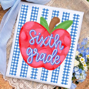 May include: A rectangular white sign featuring a blue and white gingham pattern background. Centered on the sign is a large red apple illustration with green leaves and a brown stem. The text Sixth grade is written in blue script.