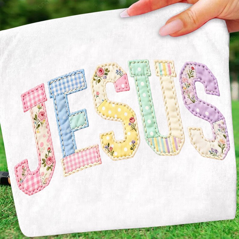Pode incluir: Tecido branco com a palavra "JESUS" aplicada em letras de patchwork coloridas. Cada letra apresenta um padr&atilde;o diferente, incluindo estampas florais, xadrez vichy e bolinhas, com uma borda costurada.
