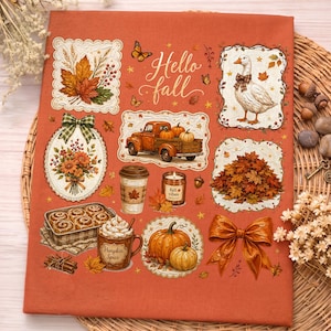 K&ouml;nnte beinhalten: Ein rostorangefarbener Stoff mit einem "Hello fall"-Aufdruck, der eine wei&szlig;e Gans, einen Oldtimer-Truck, einen Haufen Herbstbl&auml;tter, Zimtstangen, einen Pumpkin-Spice-Becher, Zimtschnecken, eine Kerze, K&uuml;rbisse und eine gro&szlig;e orangefarbene Schleife zeigt.