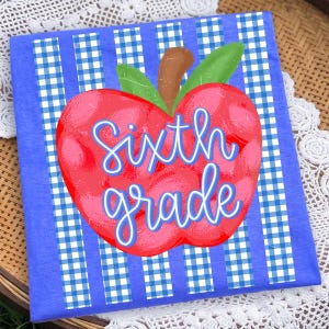 May include: A blue t-shirt featuring a red apple graphic with a brown stem and green leaves. The apple is centered over vertical blue and white gingham stripes. The text Sixth grade is written across the apple in a light blue cursive font.