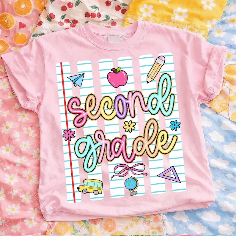 Peut inclure: T-shirt rose clair avec l'inscription "second grade" dans une police color&eacute;e et fantaisiste. Le motif comprend des graphiques sur le th&egrave;me de l'&eacute;cole, comme une pomme, un crayon, un avion en papier et un bus scolaire. Le t-shirt est en mati&egrave;re souple.