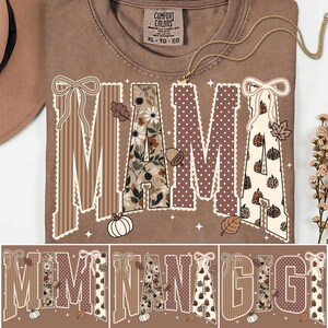 Peut inclure: Un t-shirt marron avec le mot MAMA en grandes lettres majuscules. Chaque lettre pr&eacute;sente un motif unique, notamment des rayures marron, des fleurs, des pois blancs sur fond marron et des citrouilles sur fond cr&egrave;me, avec des n&oelig;uds et des glands.