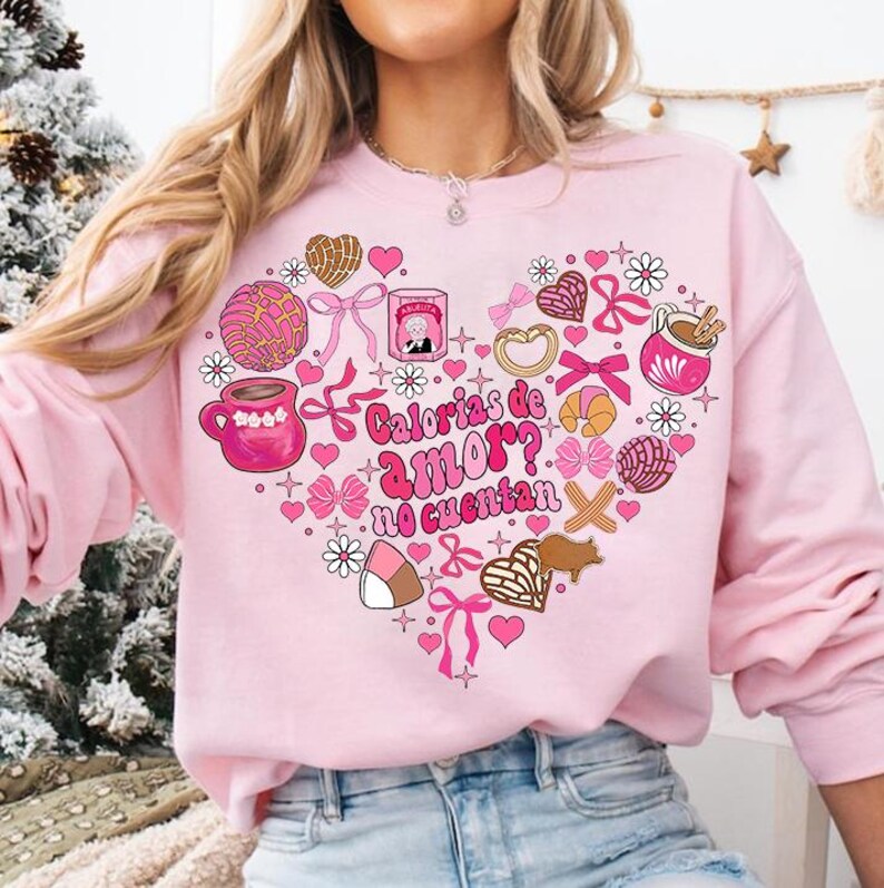 May include: Pink sweatshirt with a heart-shaped design featuring various Mexican pastries, candies, and the text "Calorias de amor? No cuentan".