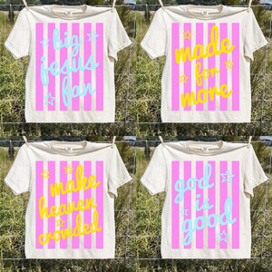 May include: Four off-white t-shirts with different phrases in colorful text. Each shirt has a pink striped background. The phrases are: "big jesus fan", "made for more", "make heaven crowded", and "god is good".
