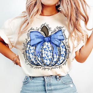 May include: A white t-shirt with a blue pumpkin design. The pumpkin has a blue bow and is surrounded by the text "Life is good.  Thankful. Grateful. Blessed. Hey pumpkin. It's fall. Y'all sweater weather."