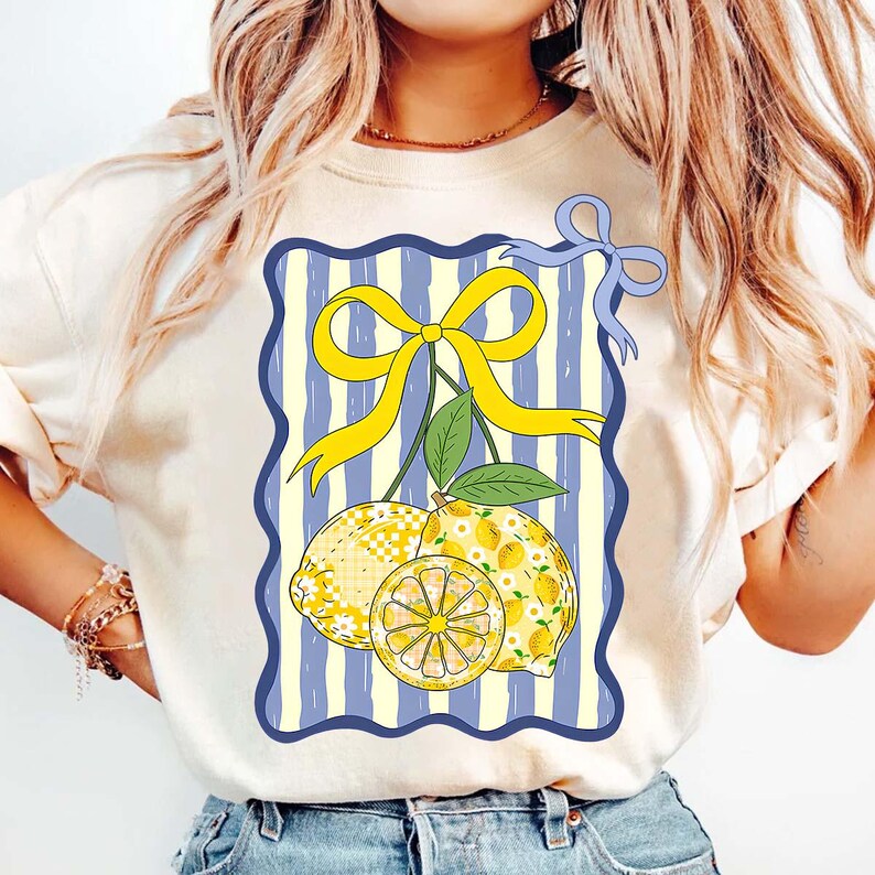 Pu&ograve; includere: Una maglietta bianca con una grafica di due limoni con un fiocco giallo su uno sfondo a righe blu e bianco.