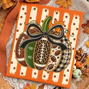 May include: A rectangular canvas print featuring a central pumpkin graphic composed of football-themed segments, including brown leather, green field markings with numbers 40 and 50, leopard print, and black buffalo plaid, topped with a black bow.