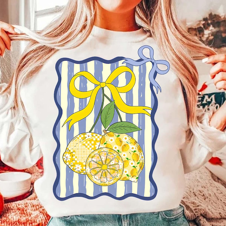 Pu&ograve; includere: Felpa bianca con una grafica di due limoni con un fiocco giallo su uno sfondo a righe blu e bianco.