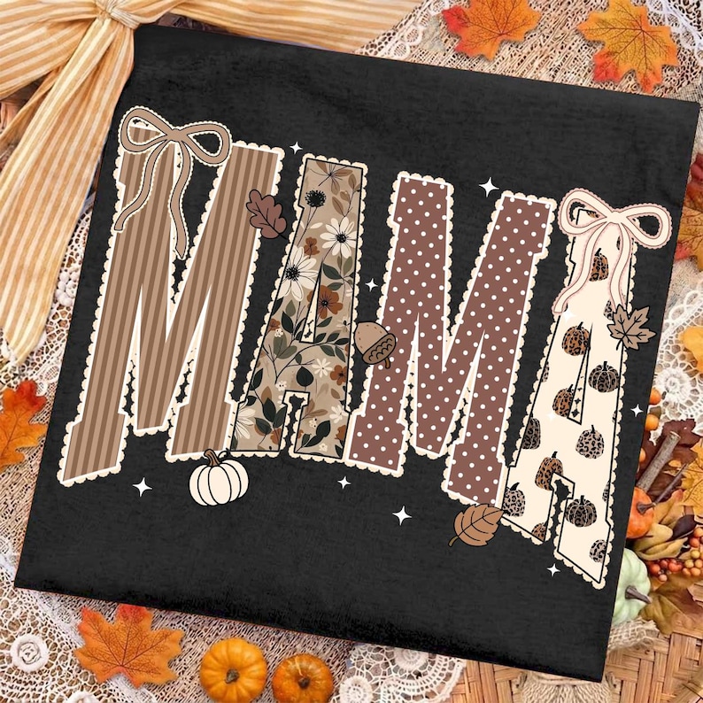 Peut inclure: Un t-shirt noir avec le mot MAMA en grandes lettres majuscules. Chaque lettre pr&eacute;sente un motif unique, notamment des rayures brunes, des fleurs, des pois bruns et des citrouilles &agrave; imprim&eacute; l&eacute;opard. Le design inclut des n&oelig;uds blancs et des &eacute;toiles.
