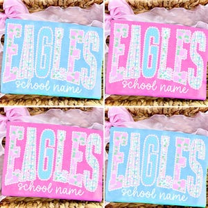 May include: Four t-shirts with the word "EAGLES" in large, decorative letters. The shirts are in shades of pink and blue, with the text in contrasting colors and a floral pattern. The words "school name" are below the main text.