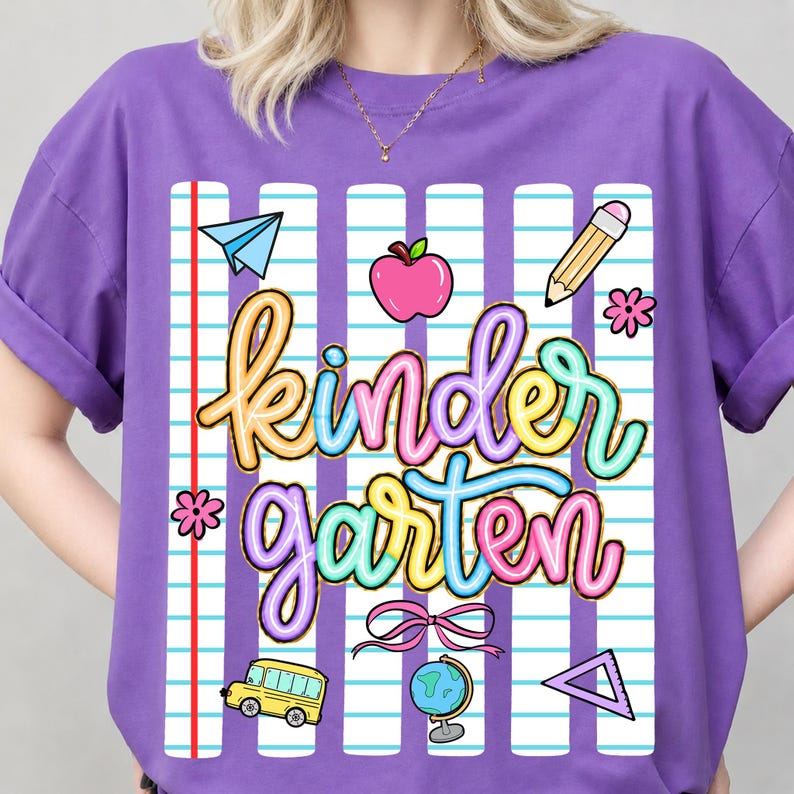 Peut inclure: Un t-shirt violet avec un motif "Kindergarten" color&eacute;. Le motif comprend un avion en papier, une pomme, un crayon, des fleurs, un bus scolaire, un n&oelig;ud, un globe et un triangle. Le t-shirt a un fond de papier de cahier.